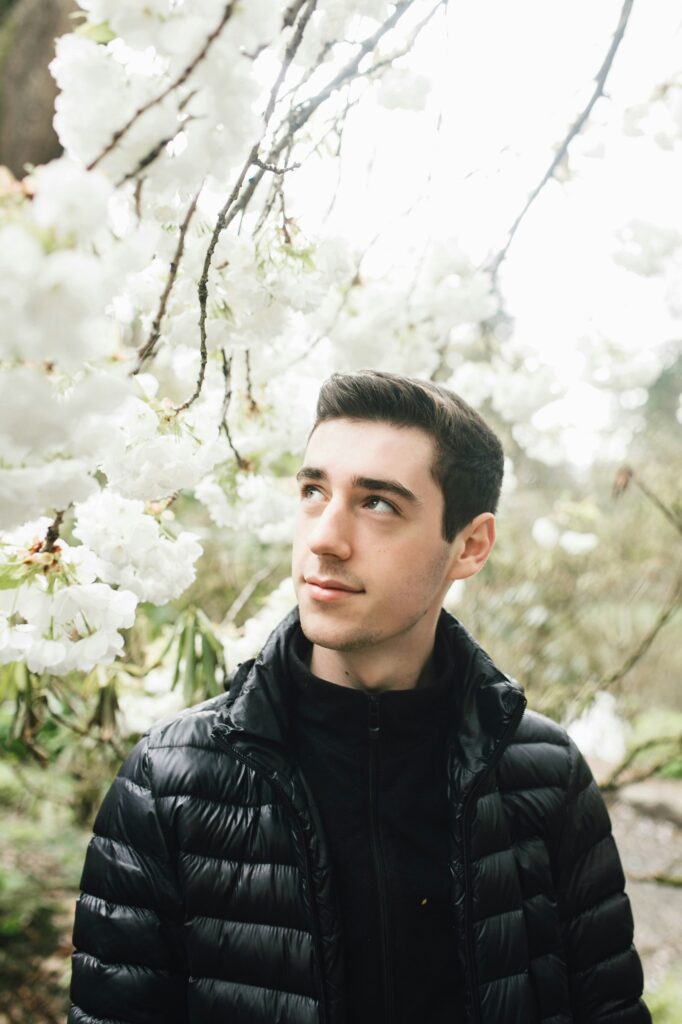 Un jeune homme regardant avec admiration les fleurs blanches en pleine floraison, entouré d'une ambiance lumineuse et naturelle, portant une veste noire matelassée.

