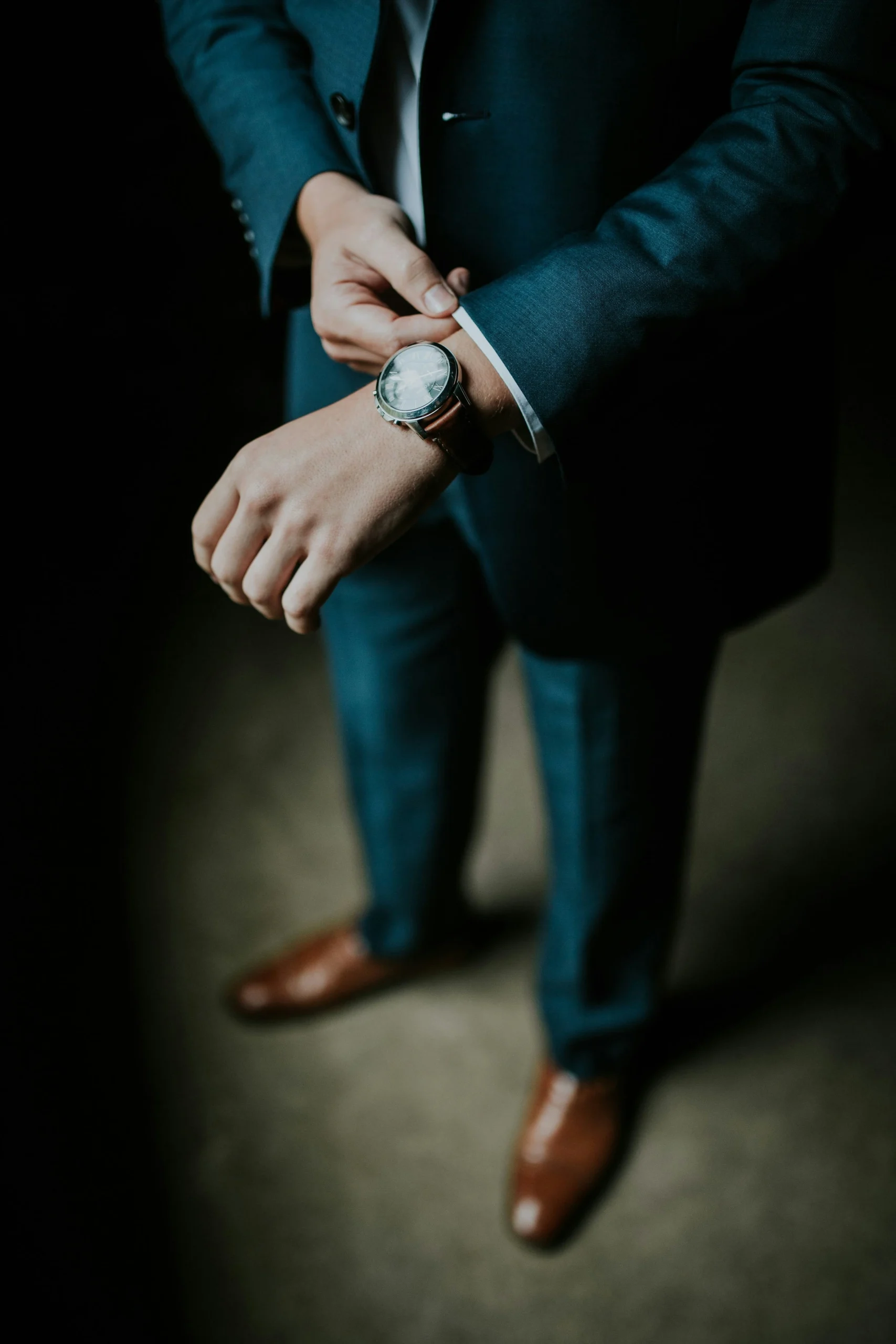 Homme vêtu d'un costume bleu ajustant sa montre-bracelet en cuir marron.