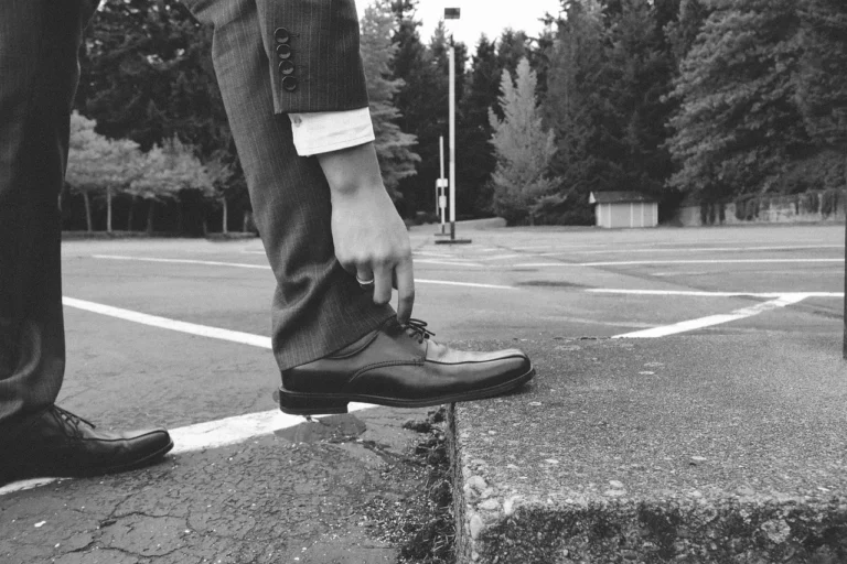 Homme ajustant ses lacets, portant un costume élégant et des chaussures en cuir noir.