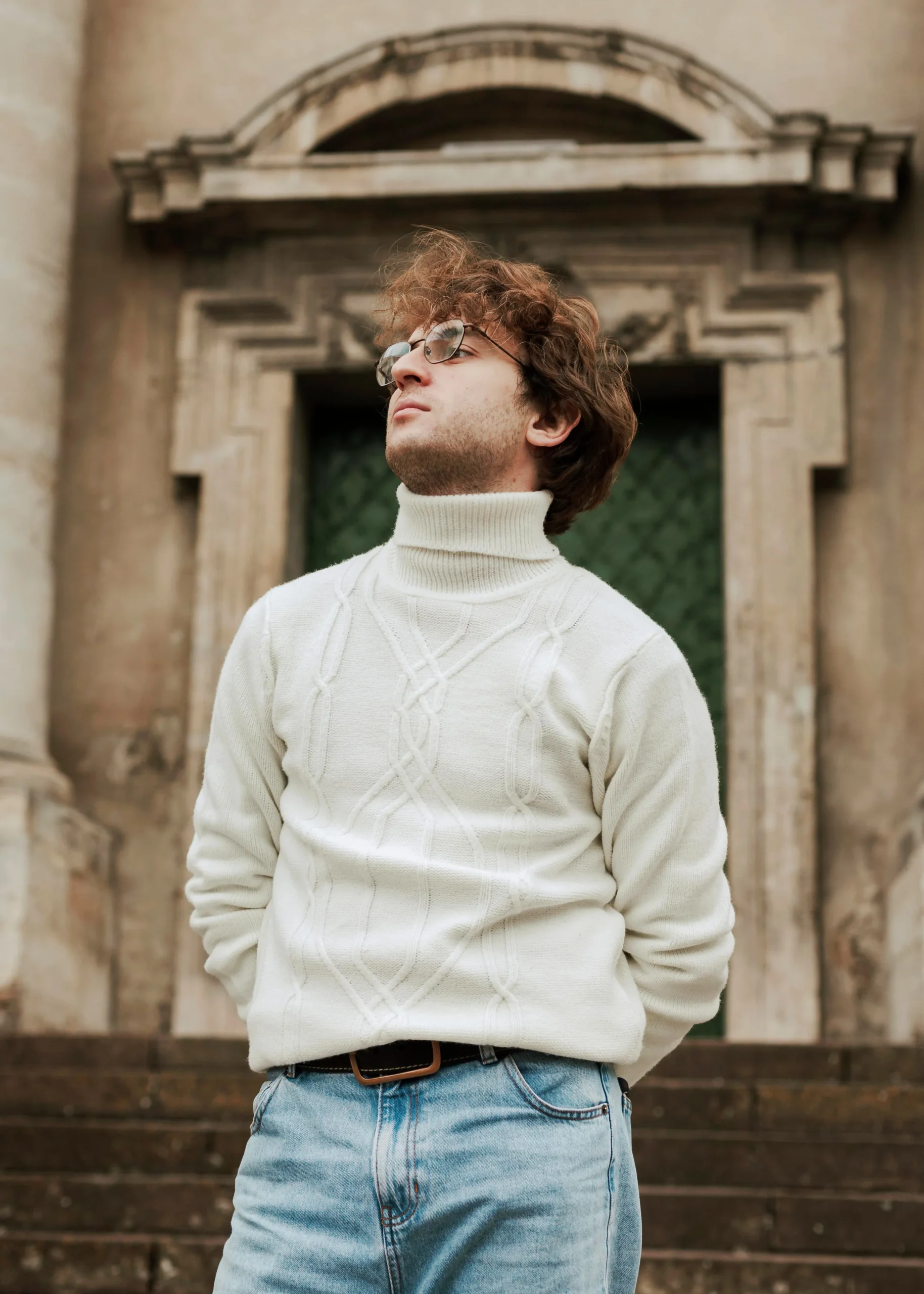 Homme portant un pull élégant avec un design moderne, posé devant un mur texturé gris.